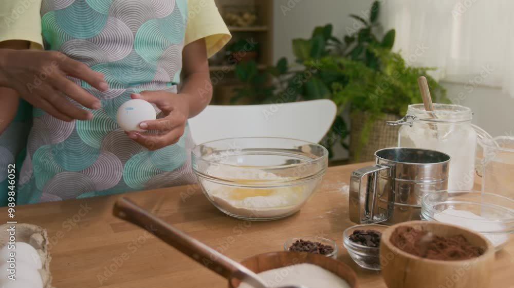Cropped shot of unrecognizable child in apron learning to crack eggs while making dough for homemade pastry, mom helping in home kitchen Cropped shot of unrecognizable child in apron learning to crack eggs while making dough for homemade pastry, mom helping in home kitchen
