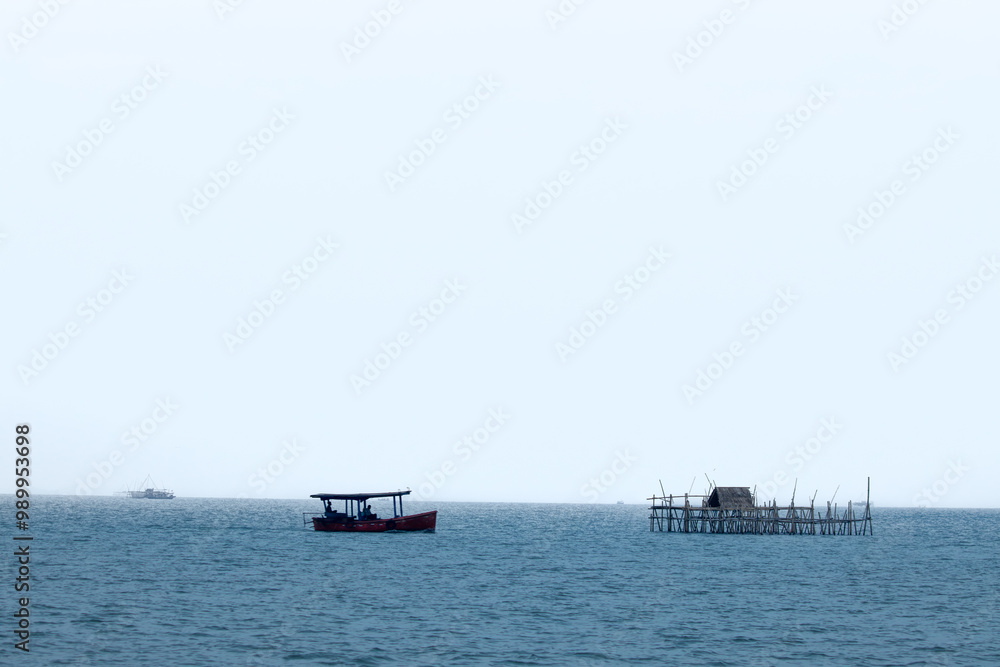 Obraz premium Bagan Apung with Fishing Boat in the Middle of the Ocean. Crystal Blue Seas Beneath a Bright and Clear Sky.