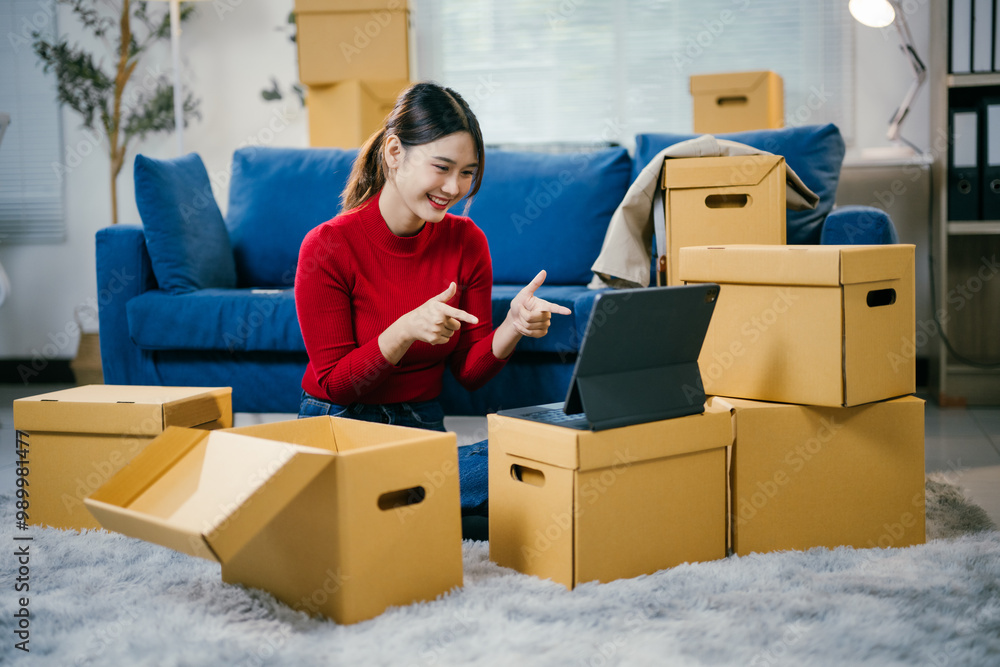 Happy woman unpacks boxes in her new home, chatting with friends online. Sitting on the floor surrounded by furniture, she uses a tablet to connect, sharing her excitement Happy woman unpacks boxes in her new home, chatting with friends online. Sitting on the floor surrounded by furniture, she uses a tablet to connect, sharing her excitement