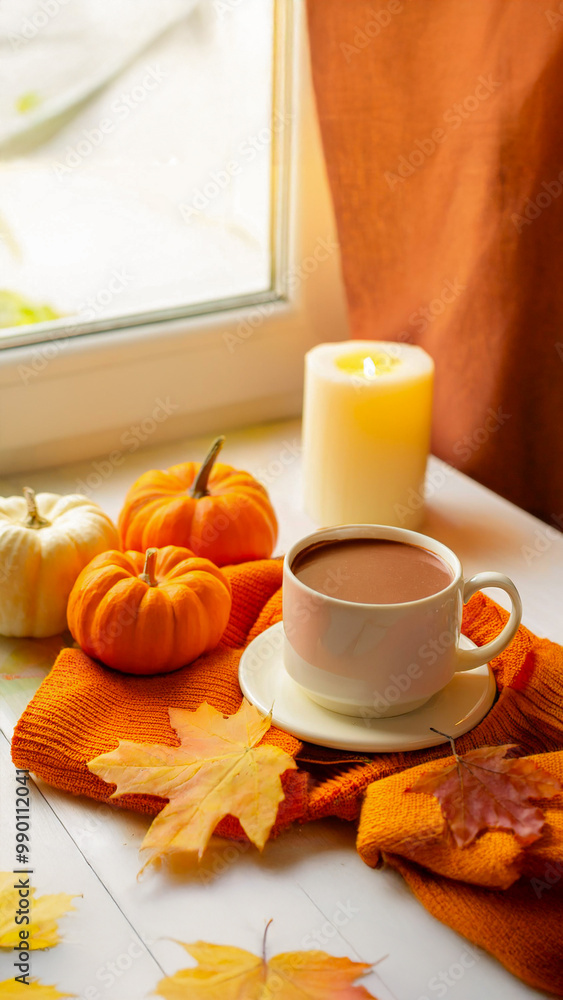 Autumn vibes cozy home: white candle, a cup of hot chocolate, maple leaves, and pumpkins on an orange clothes and white table Autumn vibes cozy home: white candle, a cup of hot chocolate, maple leaves, and pumpkins on an orange clothes and white table