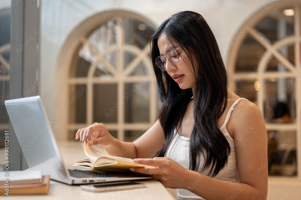An attractive Asian woman is focused on reading while working remotely from a coffee shop. An attractive Asian woman is focused on reading while working remotely from a coffee shop.