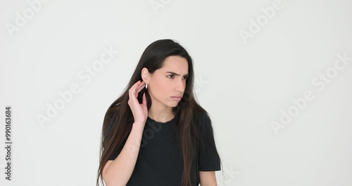 Curious woman with long loose dark hair holds hand next to ear trying to hear gossiping on white background. Female looks checking earring photo