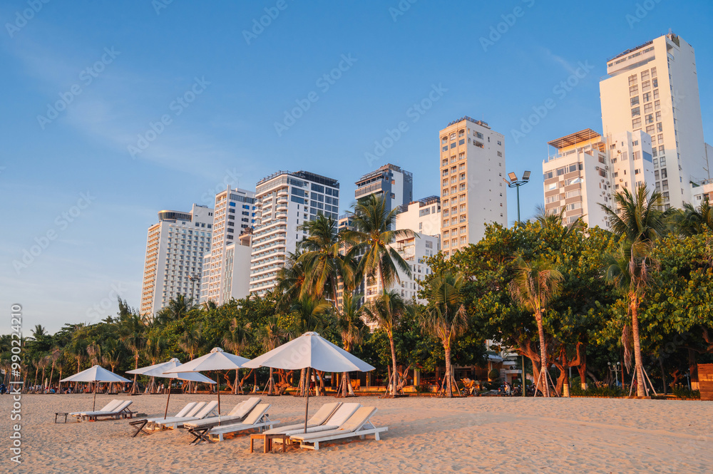 Beach umbrellas on a sandy beach by the sea in a resort town with palm trees and skyscrapers in Asia Beach umbrellas on a sandy beach by the sea in a resort town with palm trees and skyscrapers in Asia