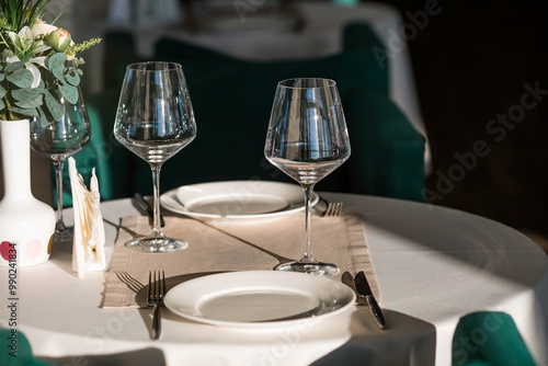 Stylish table setting. Glass glasses, plates, cutlery on the table. Wedding service, reception at the dining table. A birthday, a baptism, a festive event.