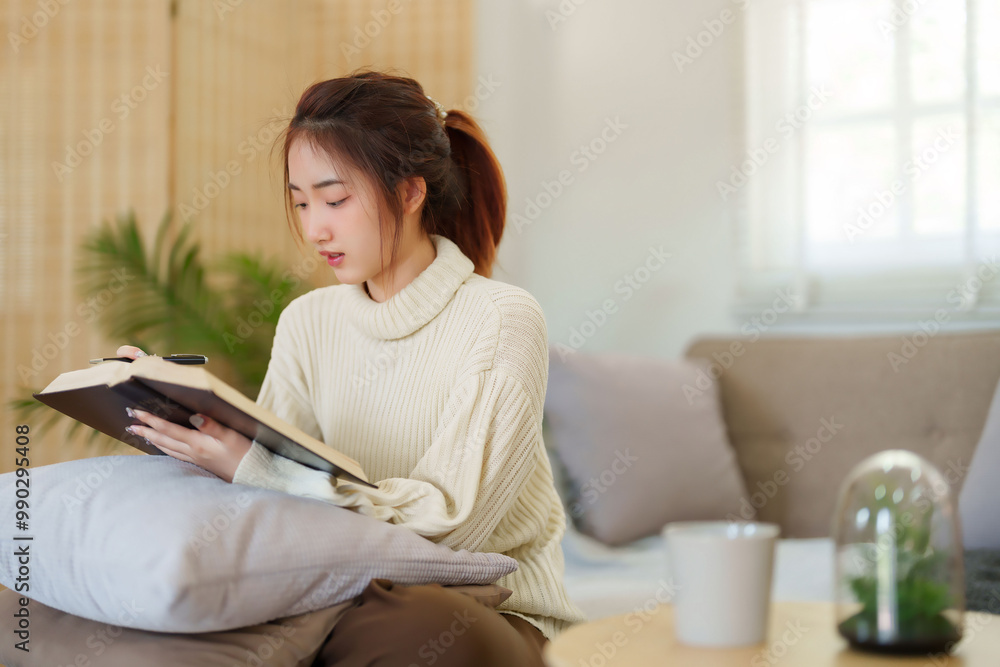 Young asian women in sweater sitting on comfortable couch and reading a book for thinking and learning education while relaxation and doing activity to spending time with slow life lifestyle at home Young asian women in sweater sitting on comfortable couch and reading a book for thinking and learning education while relaxation and doing activity to spending time with slow life lifestyle at home