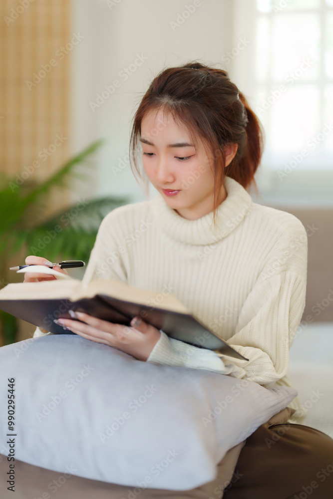 Young asian women in sweater sitting on comfortable couch and reading a book for thinking and learning education while relaxation and doing activity to spending time with slow life lifestyle at home Young asian women in sweater sitting on comfortable couch and reading a book for thinking and learning education while relaxation and doing activity to spending time with slow life lifestyle at home