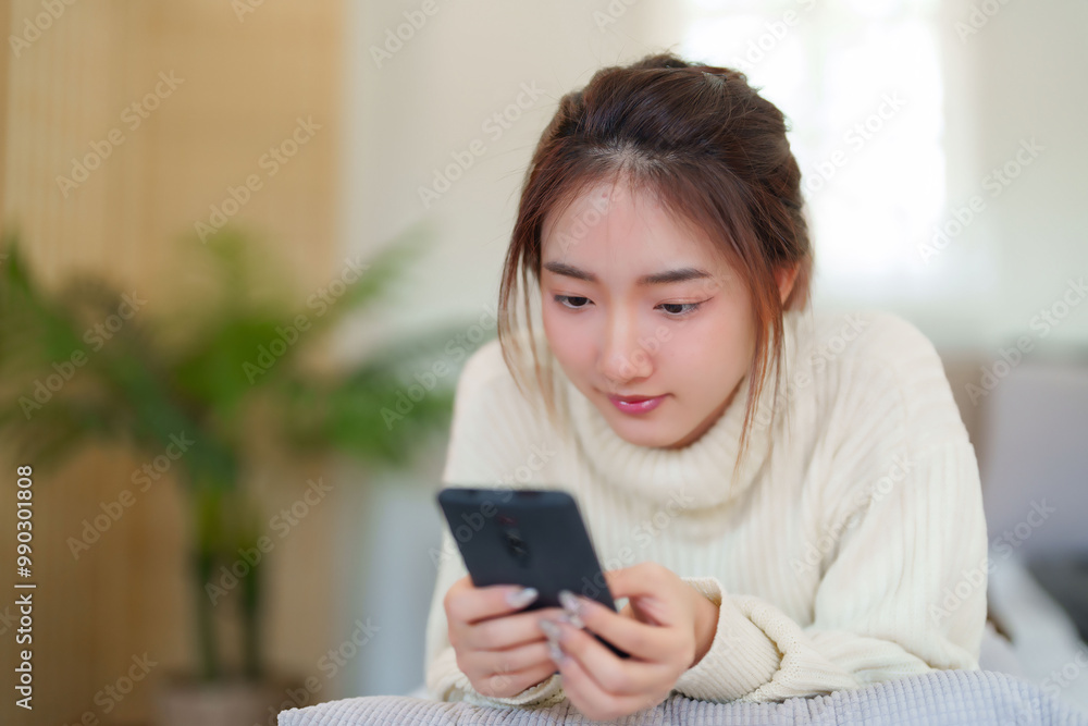 Young asian women in sweater lying on comfortable couch to enjoying with chatting social media on smartphone while relaxation and doing activity to spending time with slow life lifestyle at home Young asian women in sweater lying on comfortable couch to enjoying with chatting social media on smartphone while relaxation and doing activity to spending time with slow life lifestyle at home