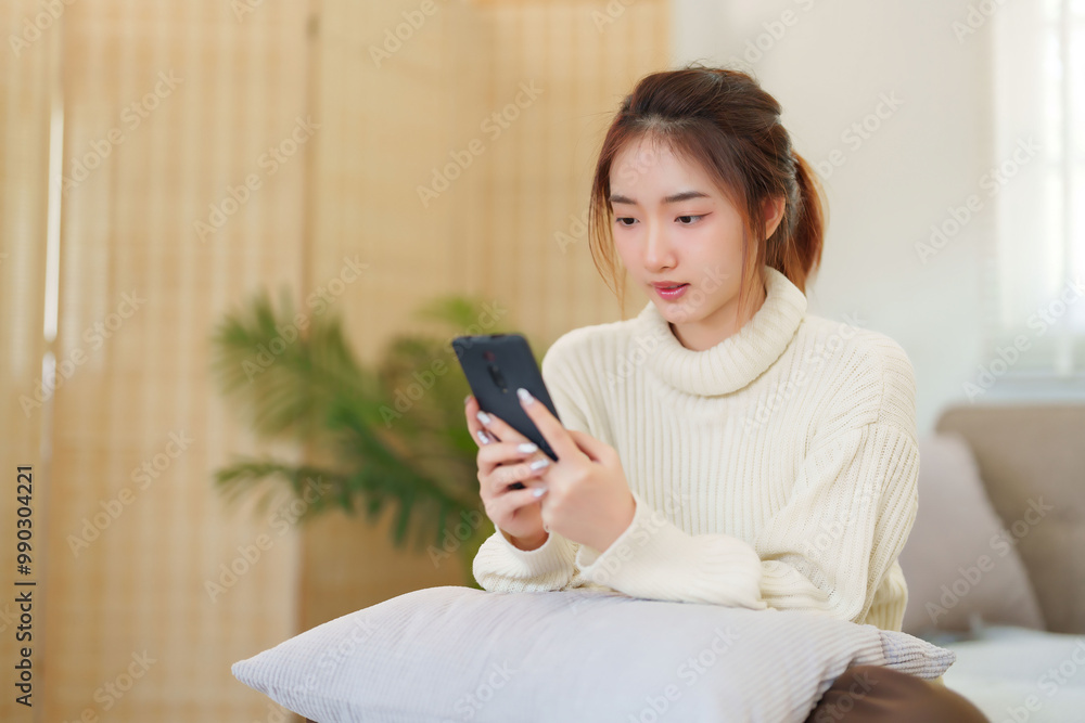 Young asian women in sweater enjoying with surfing entertainment on smartphone while sitting on comfortable couch to relaxation and doing activity for spending time with slow life lifestyle at home Young asian women in sweater enjoying with surfing entertainment on smartphone while sitting on comfortable couch to relaxation and doing activity for spending time with slow life lifestyle at home
