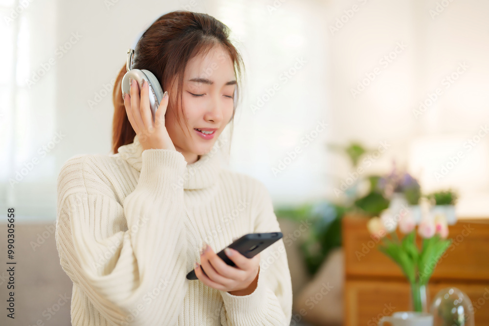 Young asian women in sweater wear headphone and listen music with enjoying on smartphone while sitting on the couch to relaxation and doing activity for spending time with slow life lifestyle at home Young asian women in sweater wear headphone and listen music with enjoying on smartphone while sitting on the couch to relaxation and doing activity for spending time with slow life lifestyle at home