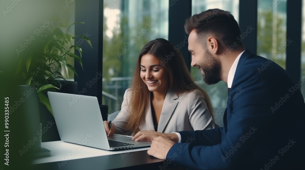 Two professionals, a man and a woman, share a happy moment while working together at a laptop in a modern office with green plants and large windows in the background. Two professionals, a man and a woman, share a happy moment while working together at a laptop in a modern office with green plants and large windows in the background.