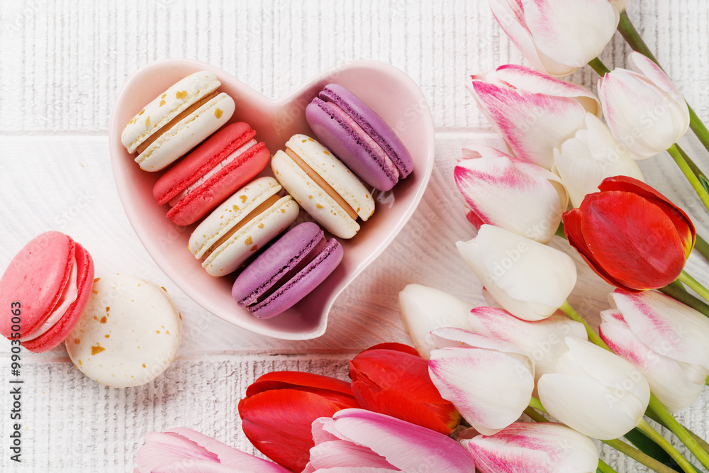 Pastel colorful tulips and vibrant macaroons fill a heart-shaped bowl Pastel colorful tulips and vibrant macaroons fill a heart-shaped bowl