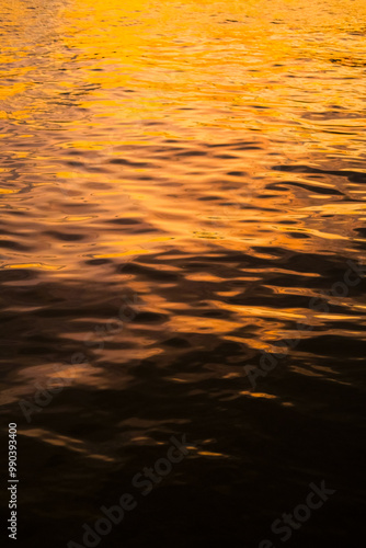 Golden reflections on rippling water create a mesmerizing texture with warm hues and dynamic patterns. Light and shadow interact, forming an abstract, tranquil, and calming natural scene.