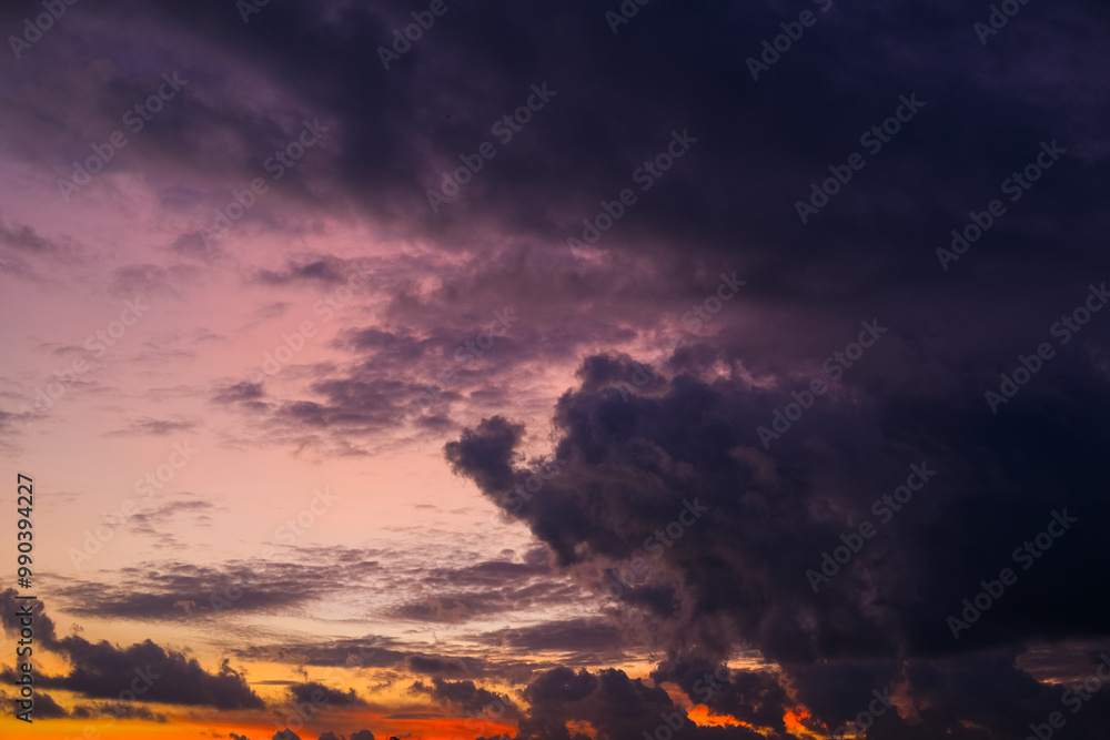 Dramatic sunset sky with vibrant orange, pink, and purple hues blending into dark clouds over a city skyline, creating a stunning contrast between light and shadow in the evening atmosphere.