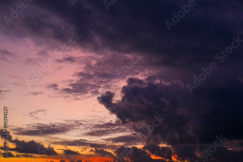 Obraz na płótnie Dramatic sunset sky with vibrant orange, pink, and purple hues blending into dark clouds over a city skyline, creating a stunning contrast between light and shadow in the evening atmosphere. w salonie