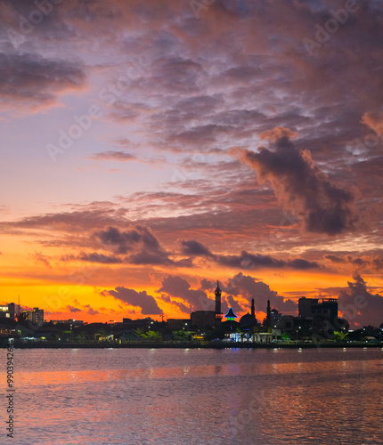 Obraz na płótnie Sunset over Kapuas River in Pontianak, illuminating the sky with orange, pink, and purple hues, reflecting on calm waters. City skyline and mosque silhouette enhance the evening scenery. w salonie
