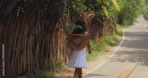 Woman Walking Down a Tropical Road with Large Palm Leaf photo