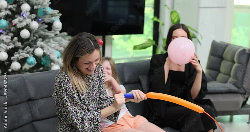 Mother and daughter happily inflate balloons with pump. Laughing women and girl prepare decorations for Christmas party creating festive atmosphere Mother and daughter happily inflate balloons with pump. Laughing women and girl prepare decorations for Christmas party creating festive atmosphere
