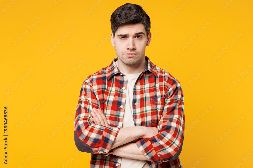 Young sad mad upset frowning grumpy man he wears red checkered shirt casual clothes hold hands crossed folded look camera isolated on plain yellow orange background studio portrait. Lifestyle concept. Young sad mad upset frowning grumpy man he wears red checkered shirt casual clothes hold hands crossed folded look camera isolated on plain yellow orange background studio portrait. Lifestyle concept.