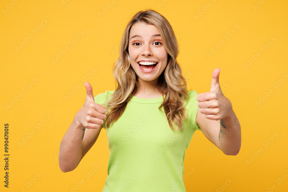 Young happy cheerful satisfied blonde woman wear green t-shirt casual clothes showing thumb up like gesture look camera isolated on plain yellow orange background studio portrait. Lifestyle concept. Young happy cheerful satisfied blonde woman wear green t-shirt casual clothes showing thumb up like gesture look camera isolated on plain yellow orange background studio portrait. Lifestyle concept.