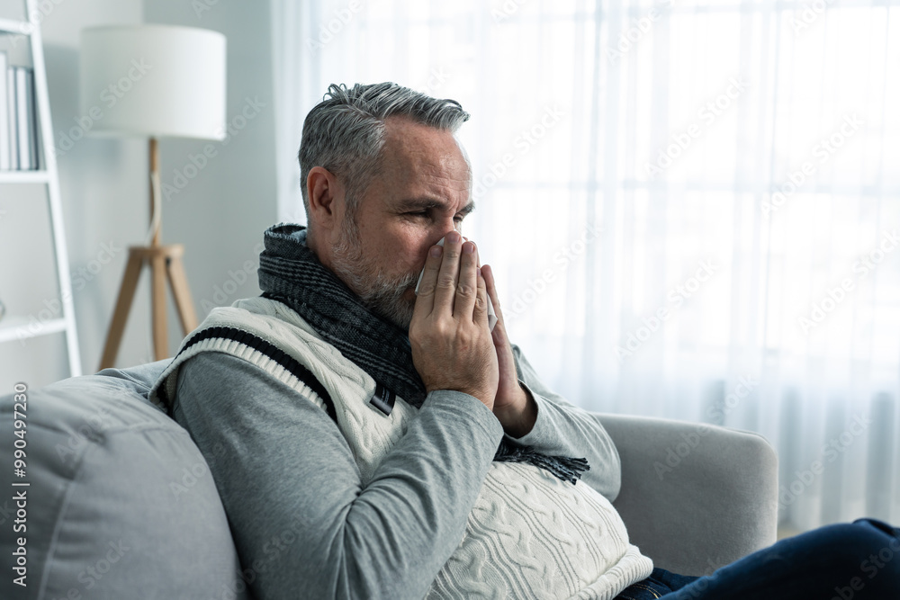 Caucasian senior man having running nose and sneezing in living room. Caucasian senior man having running nose and sneezing in living room.