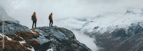 Two hikers in orange jackets admire the breathtaking snowy mountain landscape in a misty valley. Breathtaking vista , panoramic wallpaper with copy space for text.