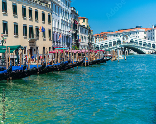 Gondoles alignées sur les quais du grand canal à Venise avec le pont du Rialto à l'arrière plan avec un grand ciel bleu et une journée ensoleillée.