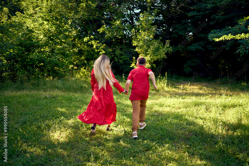 Fototapeta premium mother and preteen son in red clothes are circling and running in the garden