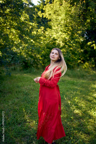 portrait of a beautiful 30-year-old woman with long blond hair in a red dress in a park