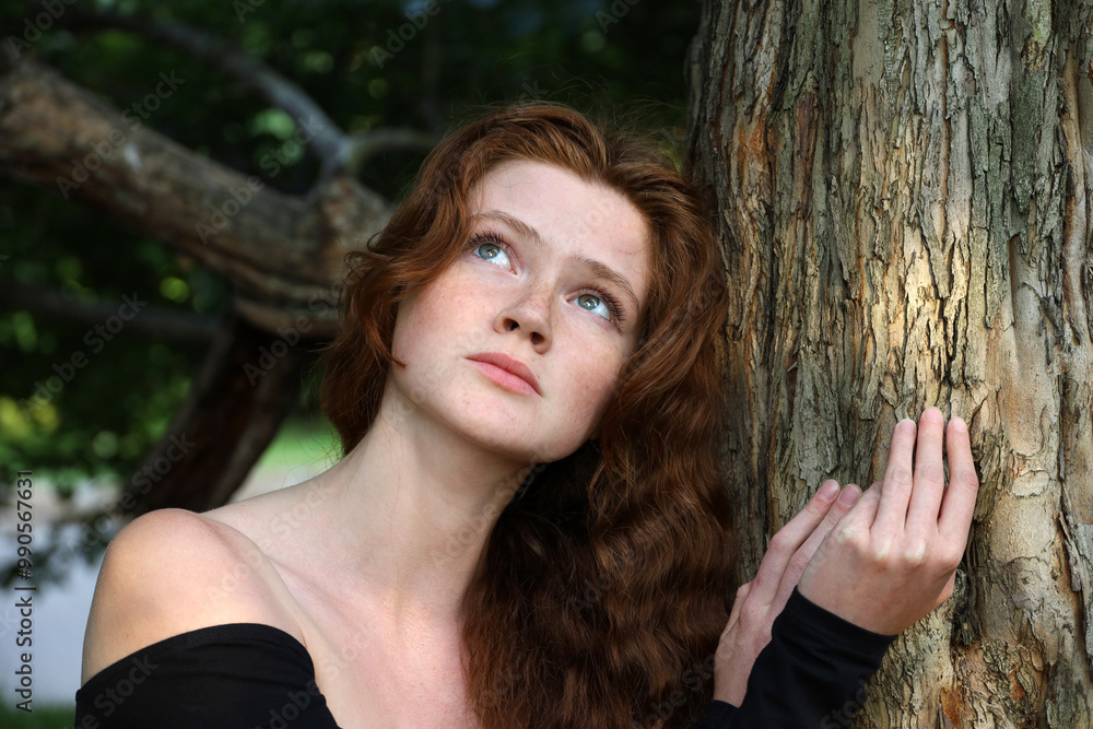 Naklejka premium Sensual close up outdoor portrait of sad ginger caucasian attractive girl with red hair and freckles near the tree