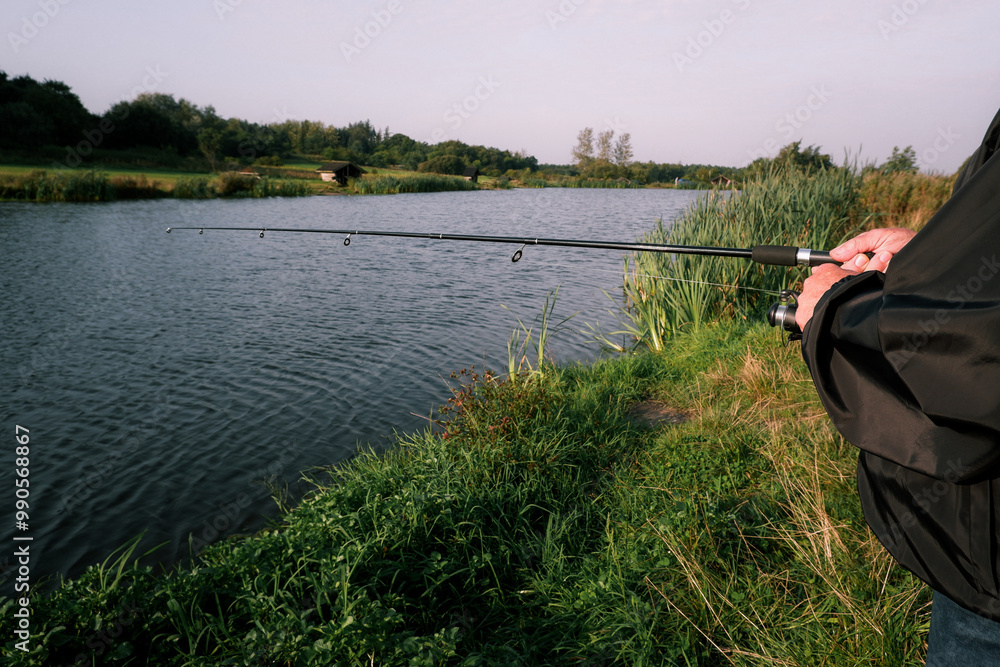 Trout fishing with spinning rod on a small lake. Fisherman fishing in a lake. Close-up of fishing rod on lake Trout fishing with spinning rod on a small lake. Fisherman fishing in a lake. Close-up of fishing rod on lake