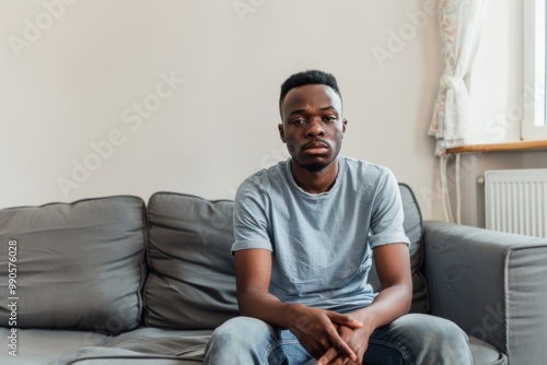 A young African-American man sits quietly on his couch, reflecting on life in the comfort of his home during a quiet afternoon