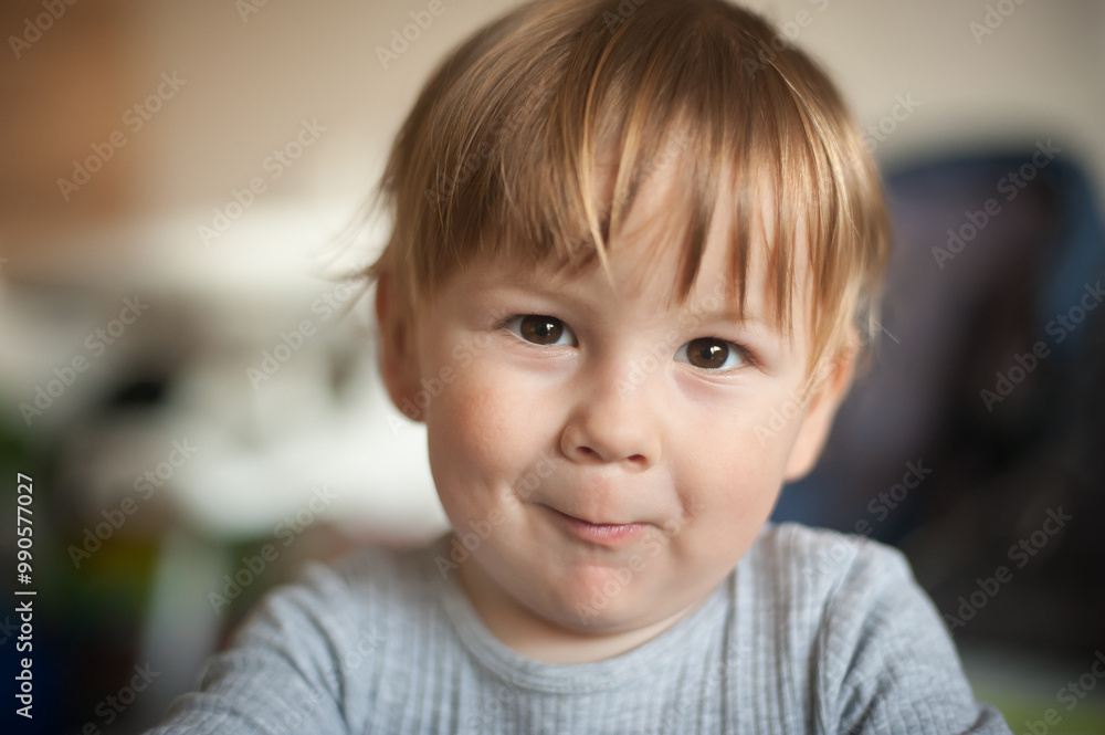A joyful toddler with tousled hair smiling warmly at the camera in a cozy indoor setting during the afternoon light A joyful toddler with tousled hair smiling warmly at the camera in a cozy indoor setting during the afternoon light