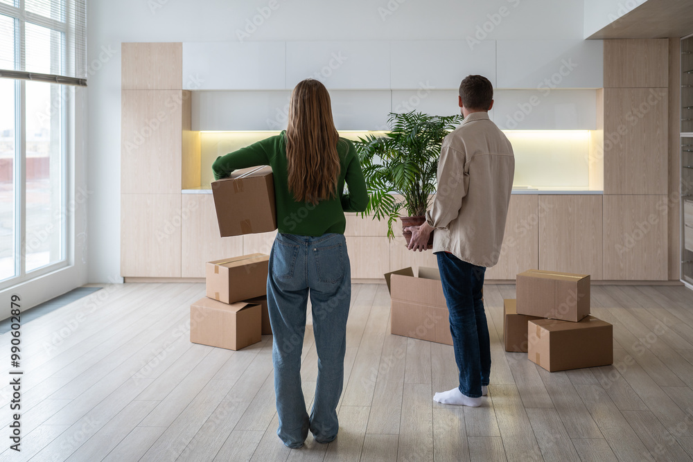 © DimaBerlin - New home owners with boxes and houseplant in hands, rear view. Family couple taking things to another rented light apartment. Housewarming in mortgage apartment. Beginning of happy married life. © DimaBerlin - New home owners with boxes and houseplant in hands, rear view. Family couple taking things to another rented light apartment. Housewarming in mortgage apartment. Beginning of happy married life.