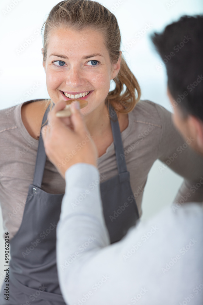 man offering woman food to taste on wooden spoon man offering woman food to taste on wooden spoon