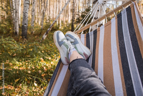 Outdoor recreation. Women's legs, shod in sneakers, in a hammock in the autumn forest. The concept of a cozy autumn vacation. photo