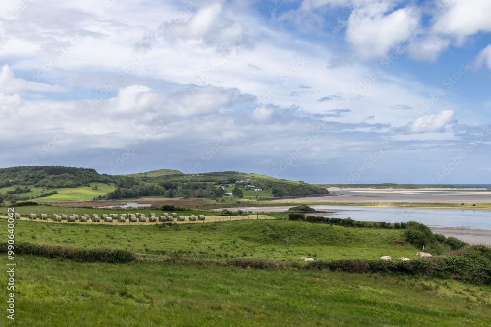 Fields and tidal shores of Gweebarra Bay, Ireland, with hay bales scattered across lush greenery and low tide exposing sandbanks Fields and tidal shores of Gweebarra Bay, Ireland, with hay bales scattered across lush greenery and low tide exposing sandbanks
