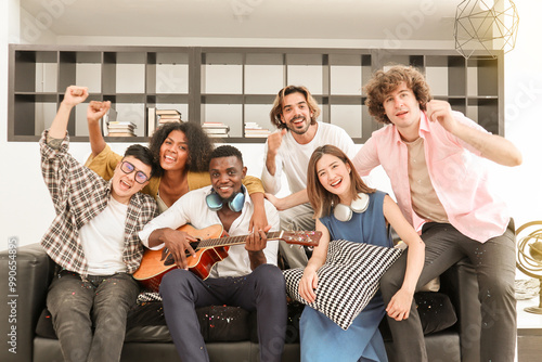 A group of multiracial teenagers playing guitar and singing a song together at the afternoon party. A group of Millennials sitting and raising their hands to celebrate the holiday weekend together.