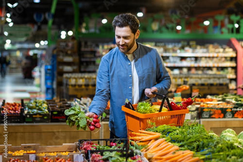 Man selecting fresh vegetables in grocery store, holding orange basket, surrounded by vibrant produce. Concept of healthy lifestyle and eco-friendly shopping in local market. Focus fresh food choice