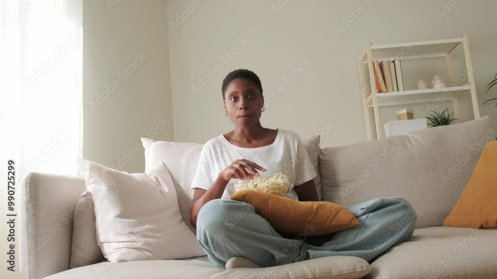 Black woman watching movie at home eating popcorn with surprise expression. 4k resolution video. Black woman watching movie at home eating popcorn with surprise expression. 4k resolution video.