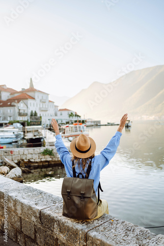 A young woman traveler enjoys the serene waterfront view in a coastal village during sunset time. Back view. Europe travel. Lifestyle, vacation, tourism, nature, active life. photo