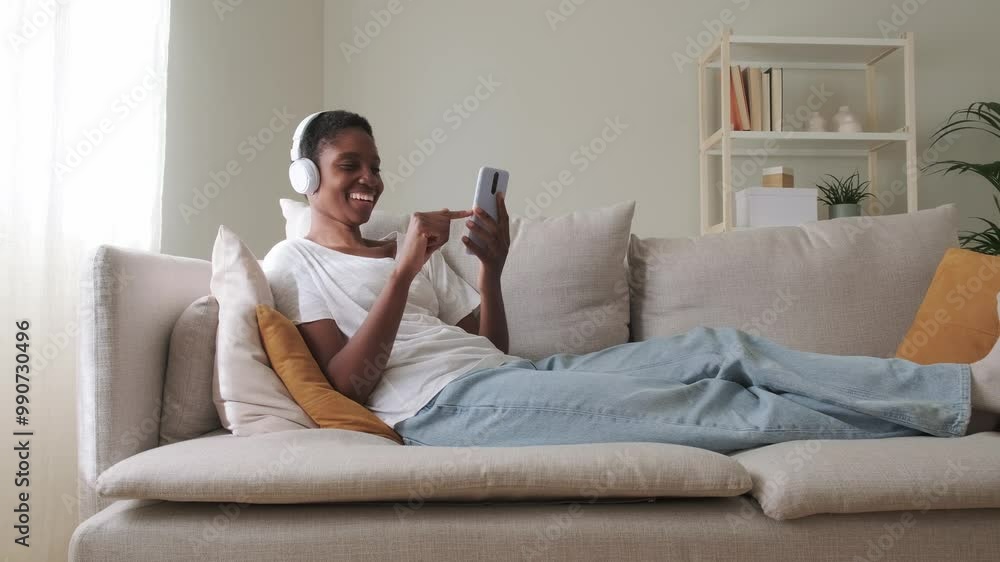 Happy Black woman relaxing on the couch using phone and headphones. 4k resolution video. Happy Black woman relaxing on the couch using phone and headphones. 4k resolution video.