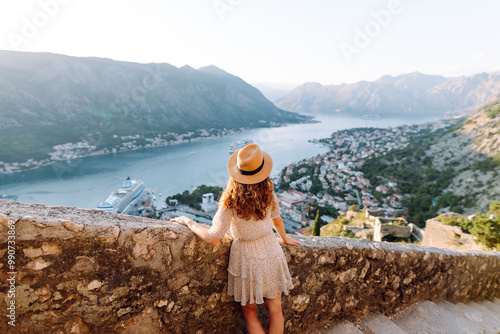 A joyful woman enjoys the stunning view of Kotor Bay from a mountain overlook on a sunny day in Montenegro. Europe travel. Lifestyle, vacation, tourism, nature, active life.