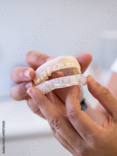 Close up of a dental professional that holds a dental mold and a clear retainer, showing them to a patient in a modern clinic setting during a consultation.