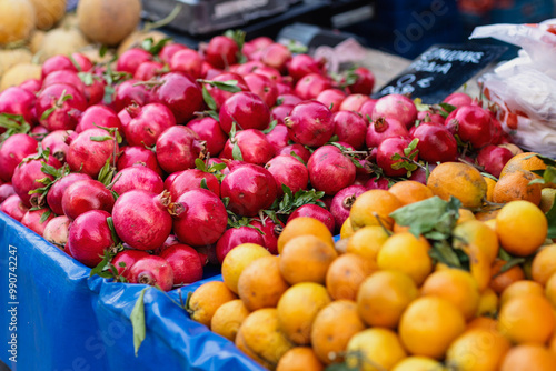Fototapeta Naklejka Na Ścianę i Meble -  Bright red pomegranates rest alongside vibrant oranges at a bustling market, showcasing the rich colors and enticing variety of fresh fruits available for shoppers to enjoy.