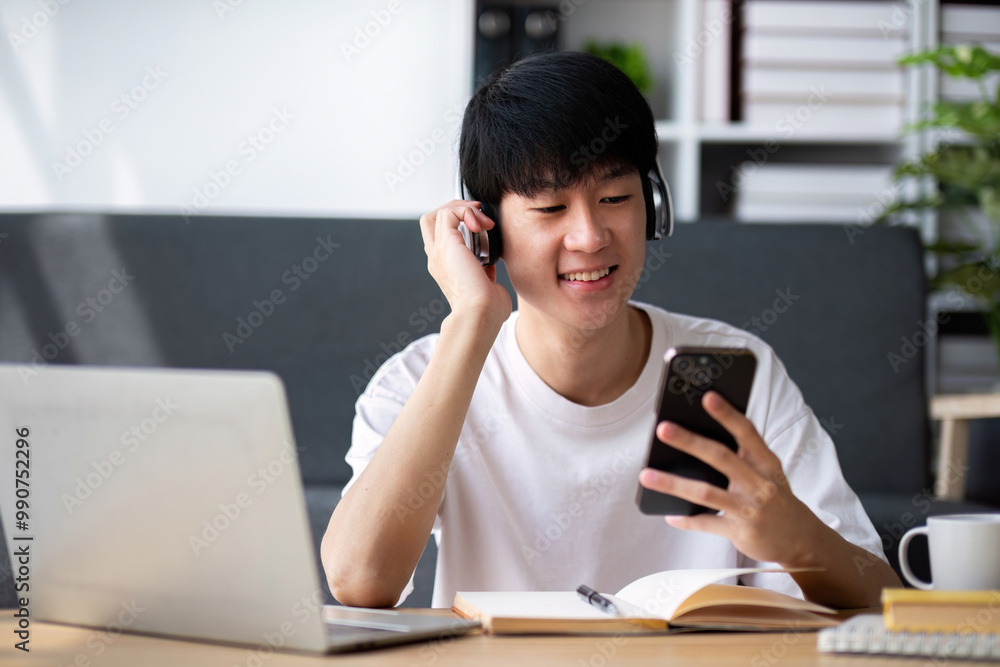 Young Boy Studying Online with Laptop and Smartphone, Engaged in E-Learning at Home, Wearing Headphones Young Boy Studying Online with Laptop and Smartphone, Engaged in E-Learning at Home, Wearing Headphones