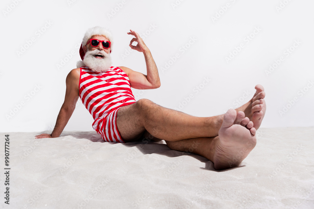 Naklejka premium Photo of positive santa claus wear red swimsuit recommend seasonal summer sale okey sign isolated on white sandy background