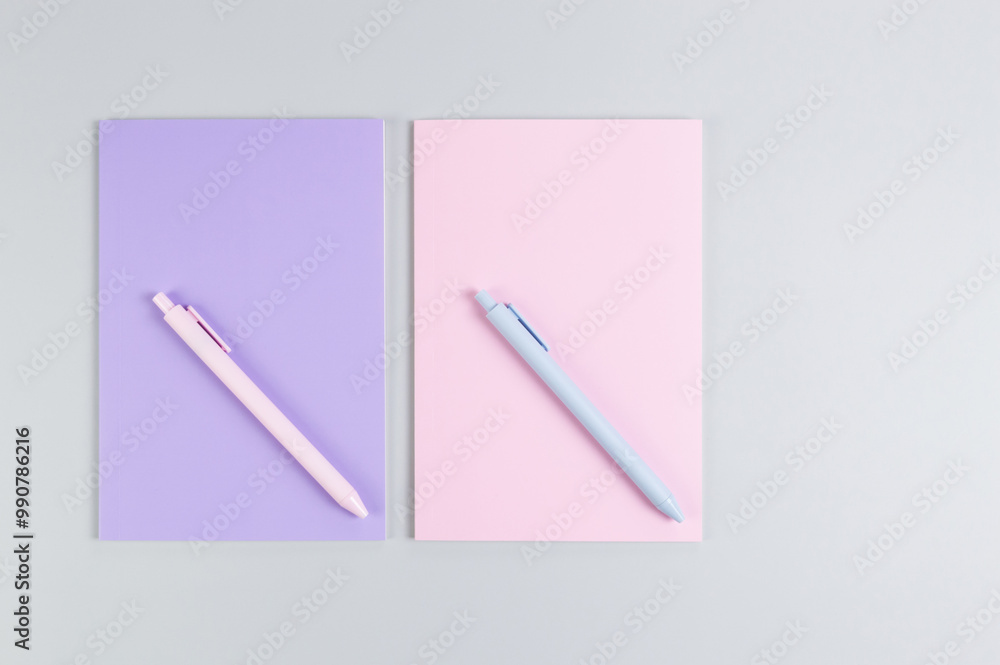Top view of pink and purple notebooks, pink and blue pens on grey background. School, office wallpaper. Flat lay, copy space. Top view of pink and purple notebooks, pink and blue pens on grey background. School, office wallpaper. Flat lay, copy space.