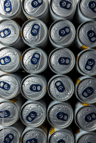 Top view of several aluminum beverage cans with blue pull tabs, covered in water droplets. The condensation emphasizes coldness and freshness, creating a sleek, metallic surface. photo