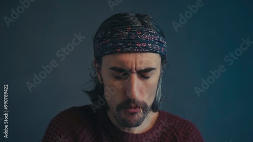 The Charismatic Hippie:rolls a toothpick with his tongue and looks down into the frame long hair. 
toothpick in mouth, mustache, headband, slomo. 