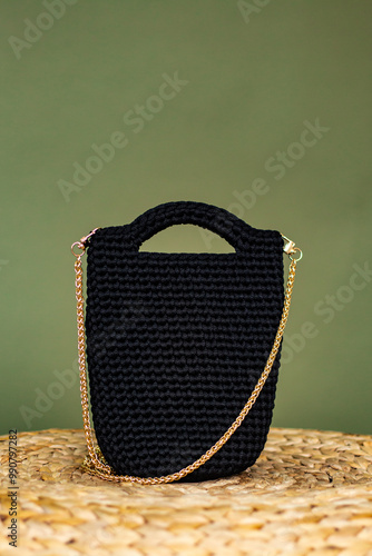 Knitted black handamde bag on the straw podium. Yarn crocheted female bag. Sustainable shopping. Eco friendly concept. photo